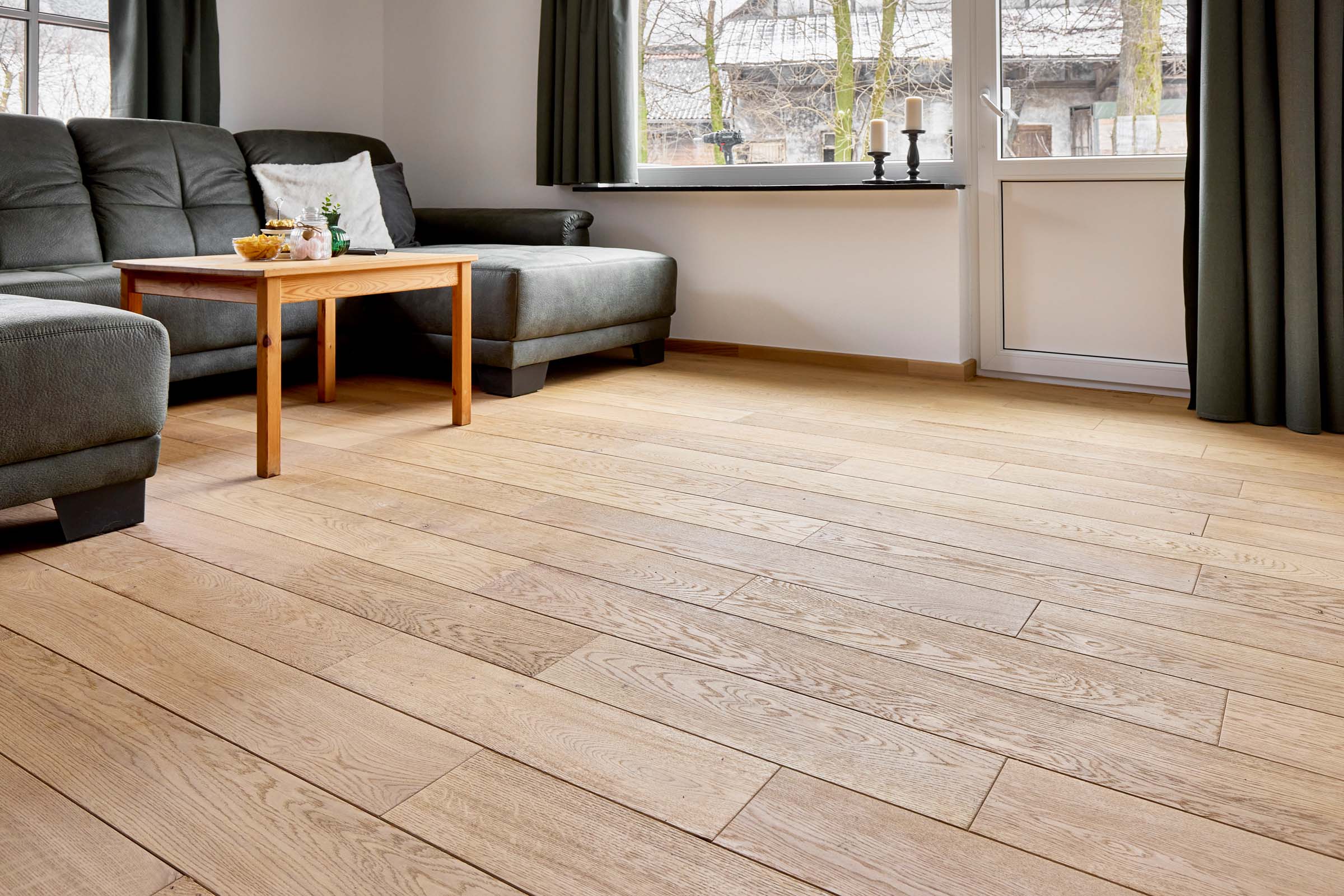Eiche-Dielenboden mit passender Sockelleiste im Wohnbereich Helles Wohnzimmer mit großformatigen Eichedielen und abgestimmter Sockelleiste – natürlicher Bodenbelag im modernen Landhausstil.